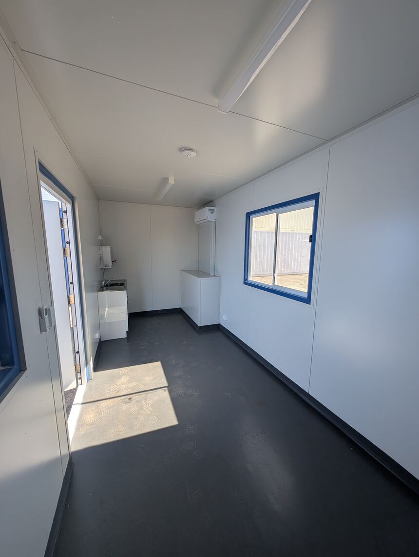 Interior of a container office looking toward the entry door, with a sink and bench