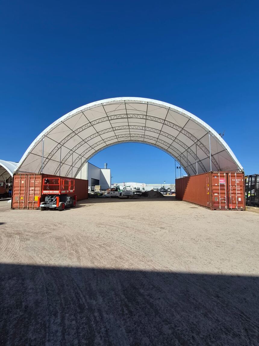 Inside a dome shelter looking out, with lighting hung from the frame and a container on precast footings