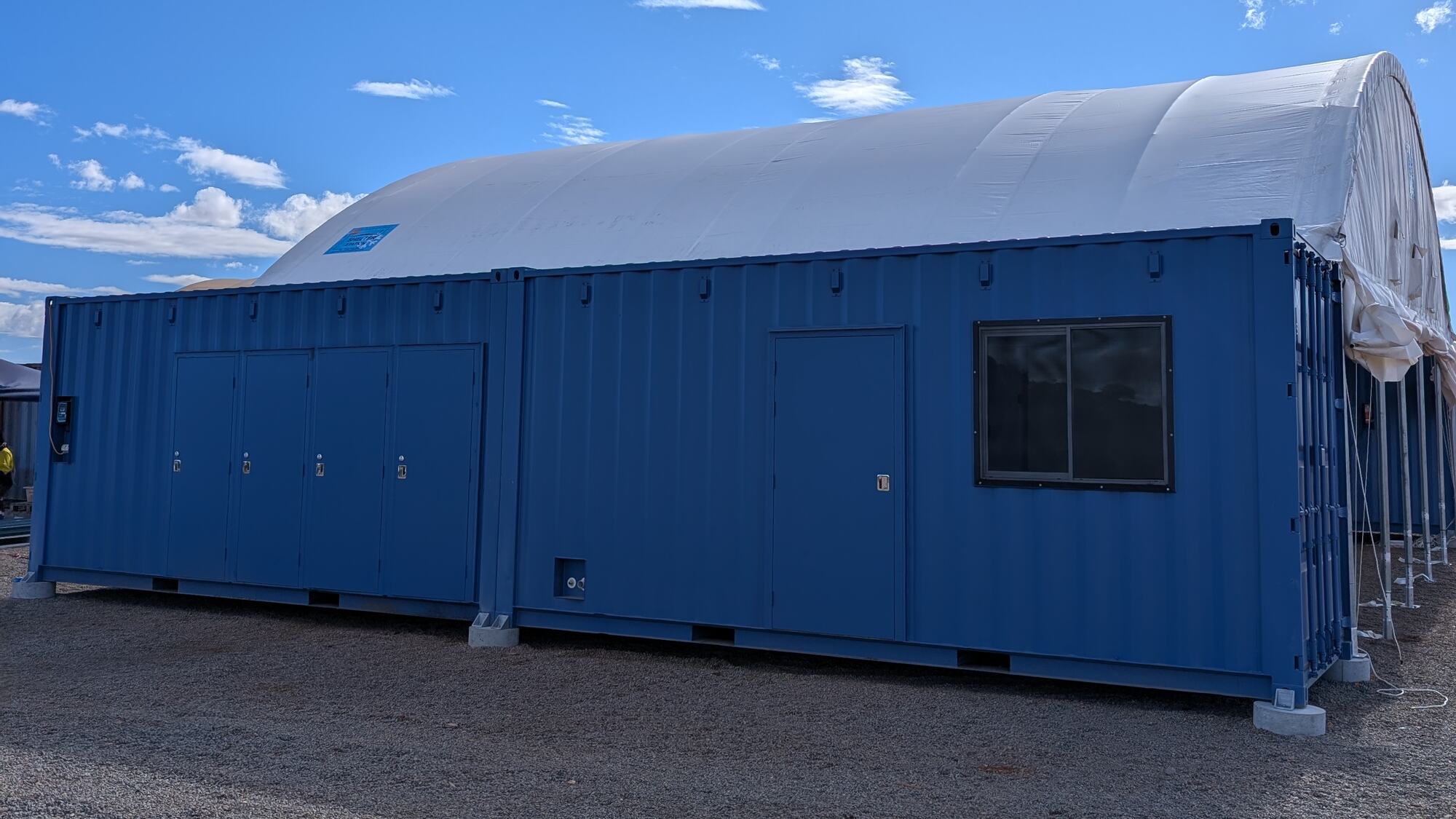 Modified shipping containers with a dome shelter installed behind them on a prepared gravel pad